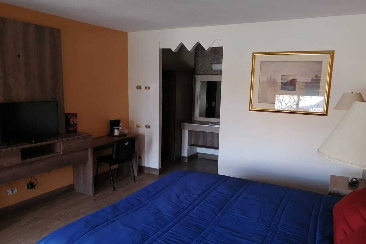 Quarto de hotel com cama, escrivaninha, televisão e espelho.