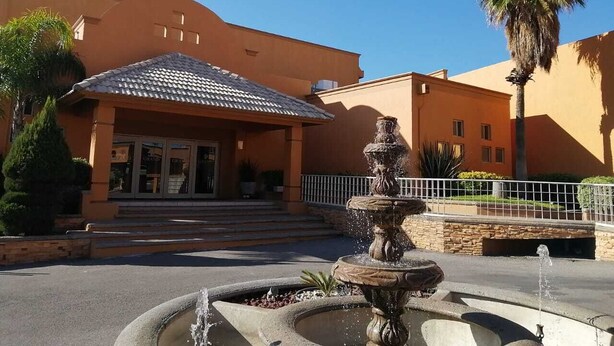 A building with a tiled roof entrance, a fountain, and a palm tree. - Hotel El Cason and Suites (Chihuahua)
