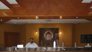 A reception desk with a wooden finish, a marble wall with a framed logo, and a bulletin board with information. - Hotel El Cason and Suites (Chihuahua)