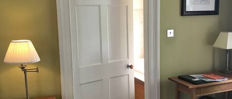 A room with a closed door, a desk with a lamp, a chair, and a framed picture on the wall.