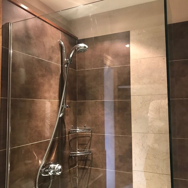 A shower with a handheld showerhead and a wall-mounted control panel.