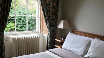 A bedroom with a bed, a nightstand, a lamp, and a window with curtains.
