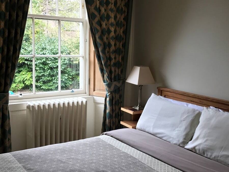 A bedroom with a bed, a nightstand, a lamp, and a window with curtains.
