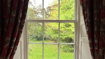 A room with a large window, white radiator, and a bed with patterned bedding.