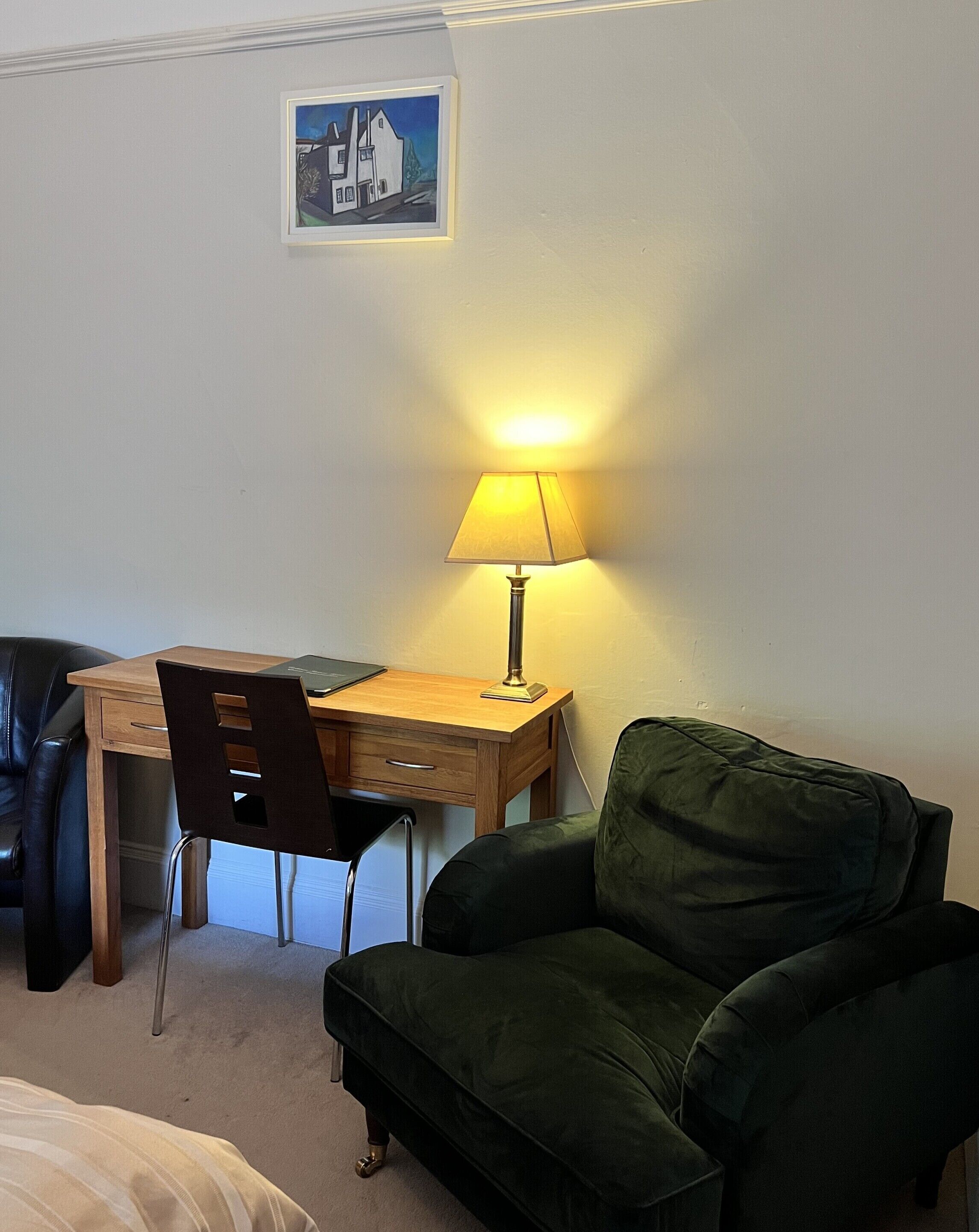 A room with a wooden desk, a green chair, a lamp, a black leather chair, and a bed.