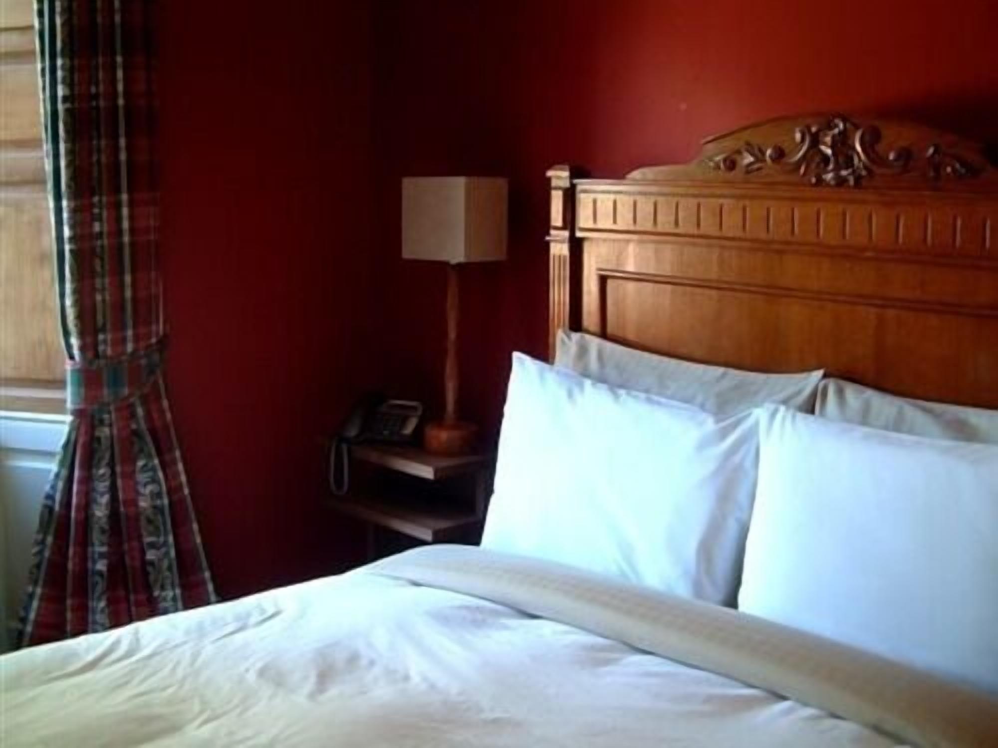 A hotel room with a wooden headboard, white bedding, a bedside lamp, and a telephone on a nightstand.