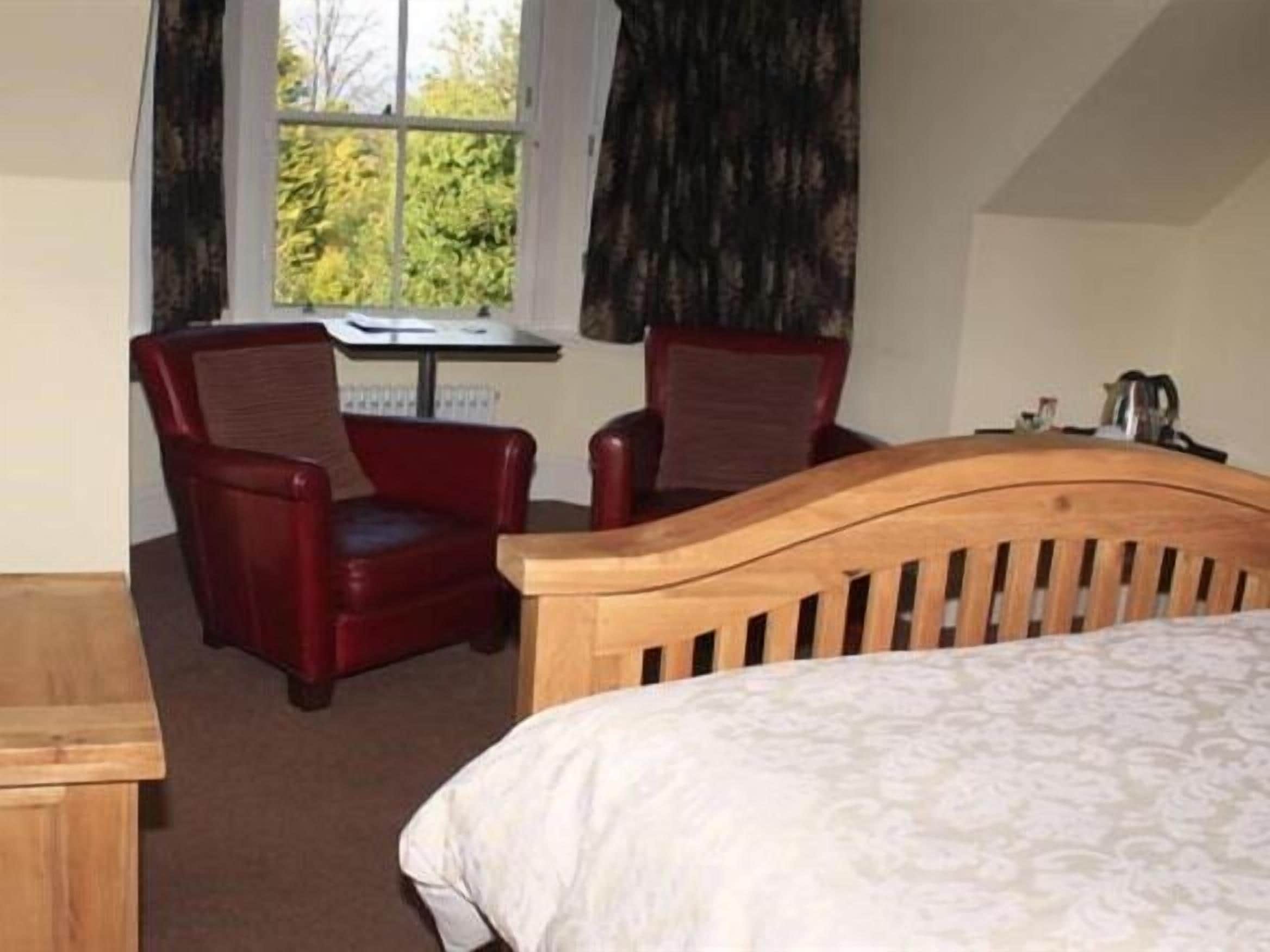 A hotel room with a wooden bed, two red chairs, a small table, and a window with curtains.