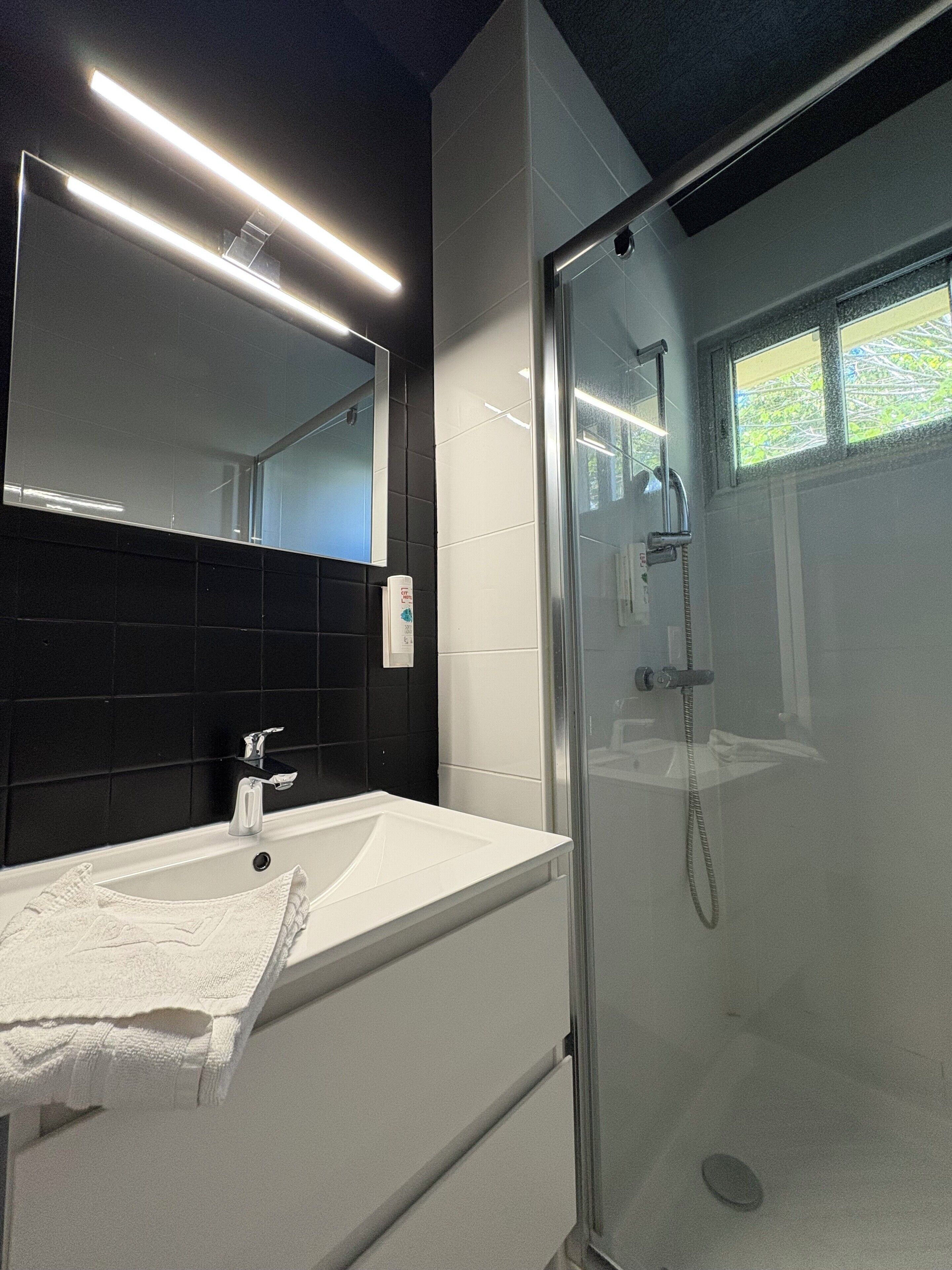 Un baño moderno con lavamanos blanco, un espejo grande y cabina de ducha con mampara de vidrio.