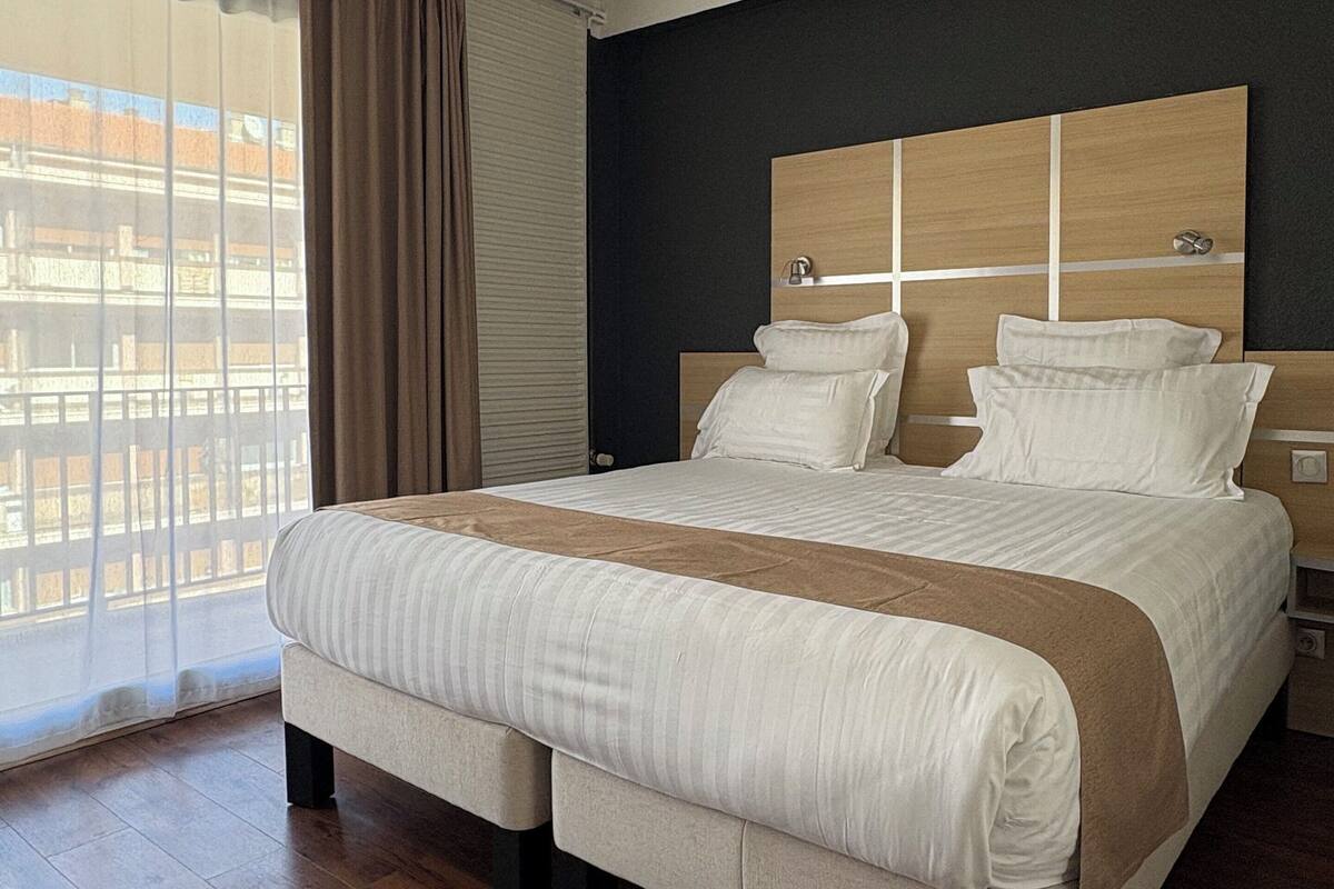 Habitación de hotel moderna con una cama grande, piso de madera y vista a la ciudad a través de la ventana.