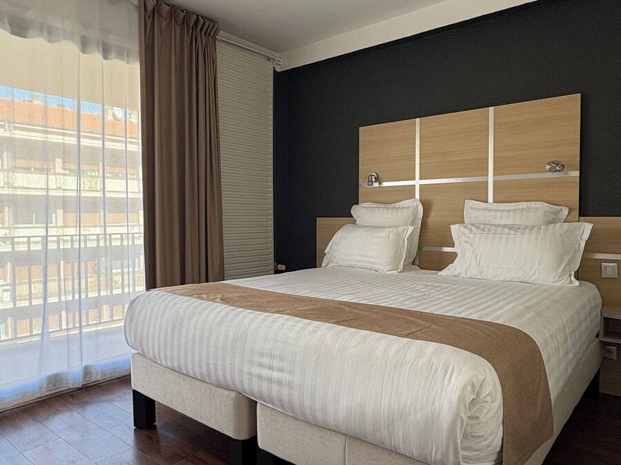 A modern hotel room with a large bed, wooden floor, and a view of the city through the window.