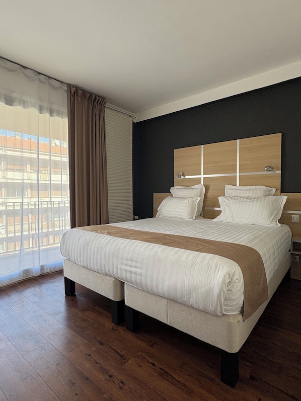 Habitación de hotel moderna con una cama grande, piso de madera y vista a la ciudad a través de la ventana.