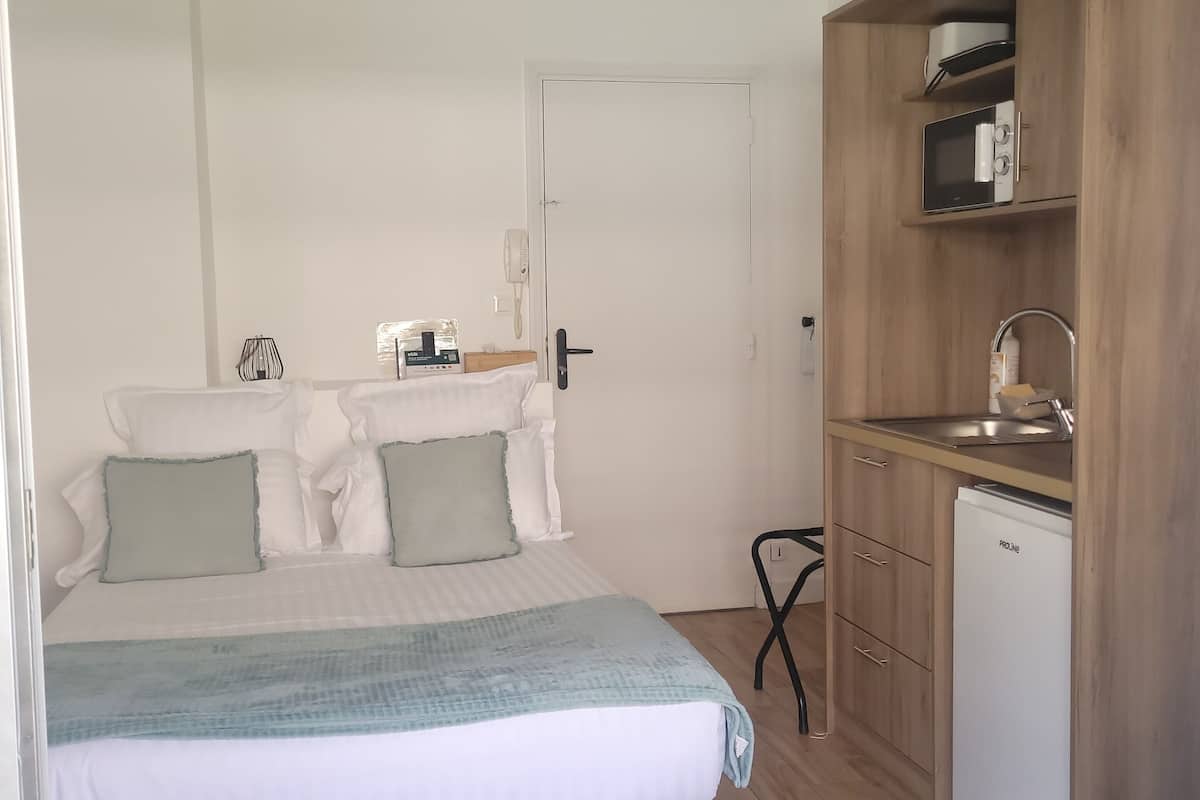Un dormitorio con cama, mesita de noche y una pequeña kitchenette equipada con microondas y refrigerador.