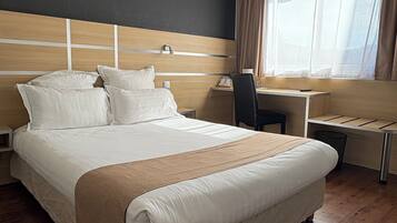 A hotel room with a large bed, a desk, and a chair.