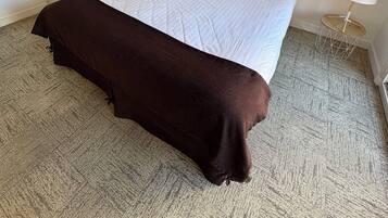 A hotel room with a large bed, a brown throw blanket, a side table with a lamp, and a curtain.