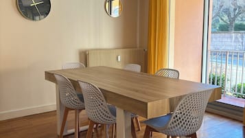 Un comedor con una mesa de madera y cuatro sillas, un reloj de pared, un espejo y una ventana con cortinas amarillas.