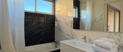 A modern bathroom with a marble vanity, a bathtub, and a large mirror.