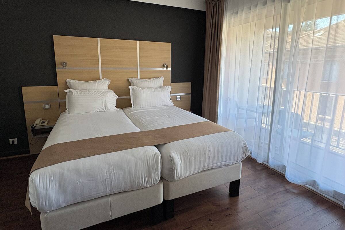 Una cama doble con cabecera de madera, ropa de cama blanca y una manta marrón.