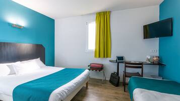 A hotel room with a large bed, a smaller bed, a desk with a chair, a TV mounted on the wall, and a window with curtains.