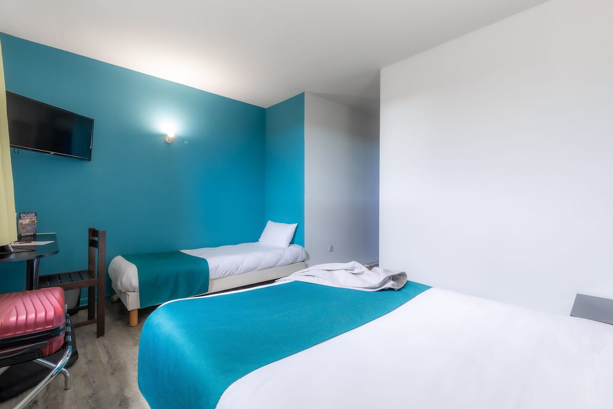 Une chambre d’hôtel avec deux lits, un bureau, une chaise, une télévision et une valise.