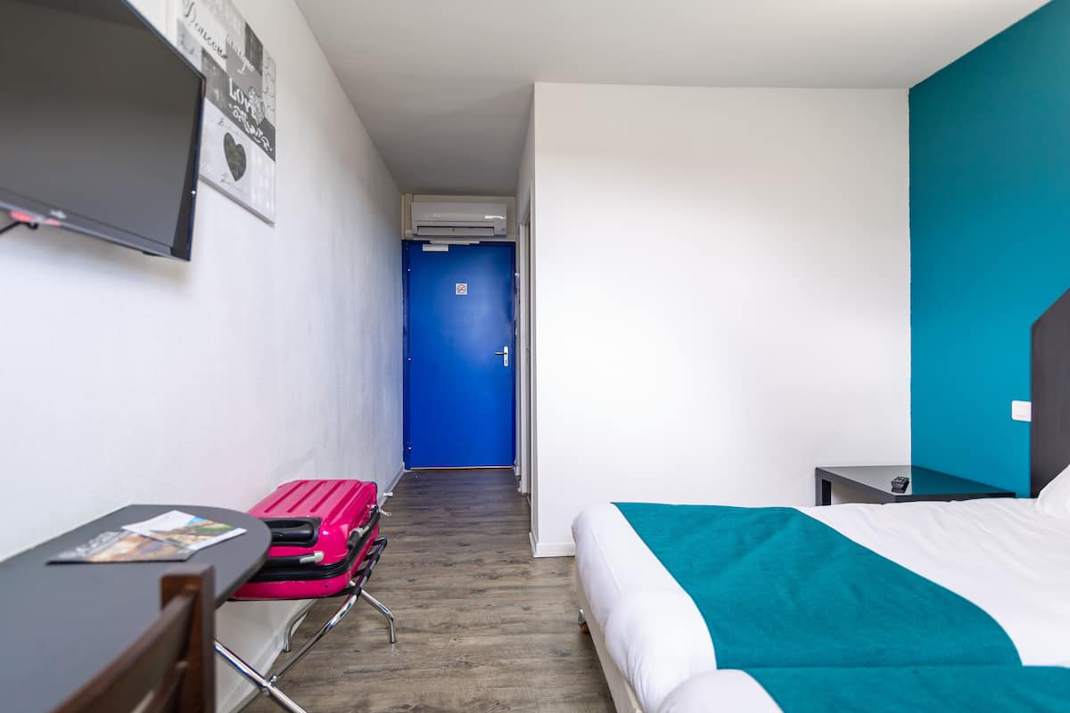 Une chambre d’hôtel avec un lit, un bureau, une chaise, une télévision et une porte bleue.