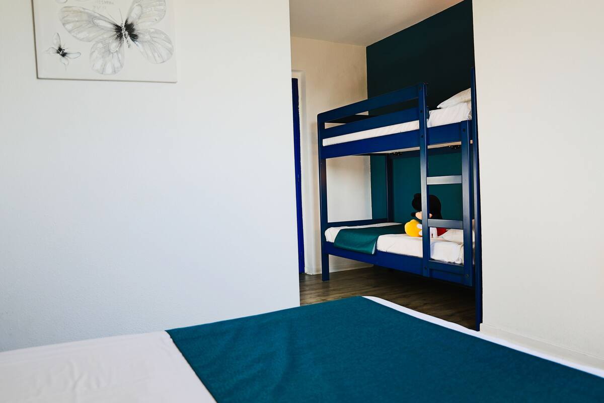 Une chambre avec un lit superposé, un mur blanc et une œuvre d’art représentant un papillon, encadrée.