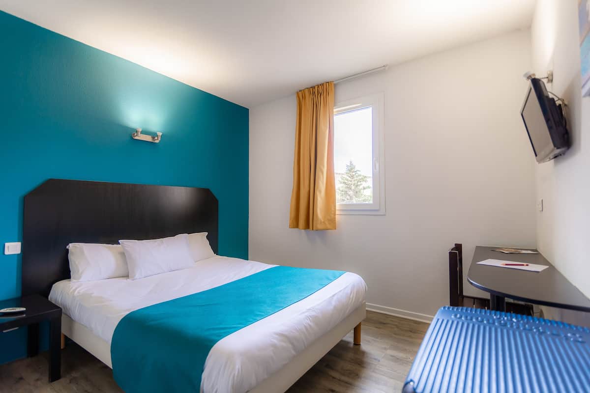 Une chambre d’hôtel avec un lit, un bureau et une fenêtre avec des rideaux.