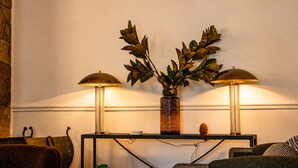 A room with a console table, two lamps, a decorative vase with foliage, and a stone wall. - Hotel St. Moritz (Lake Placid)