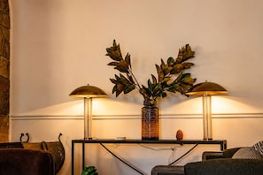 A room with a console table, two lamps, a decorative vase with foliage, and a stone wall. - Hotel St. Moritz (Lake Placid)
