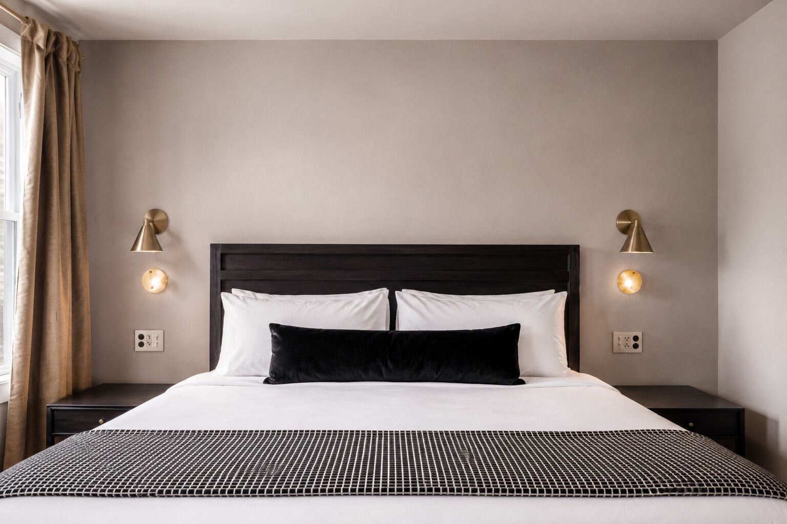 A neatly made bed with a black headboard and white bedding, flanked by two bedside lamps and a power outlet on each side.