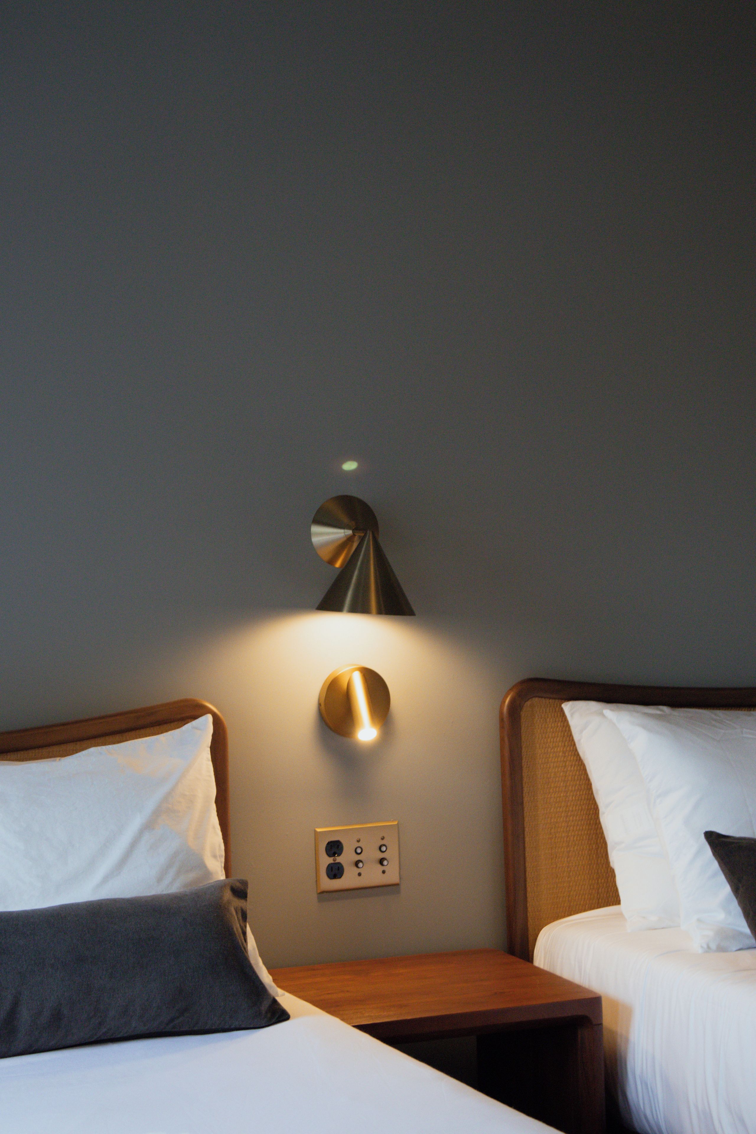 A hotel room with two beds, a wall-mounted light fixture, and a power outlet.