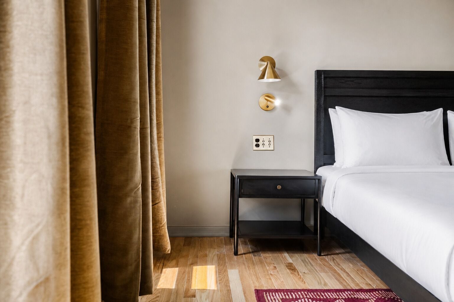 Una camera d'albergo con un letto, un comodino, una lampada a parete e una presa di corrente.