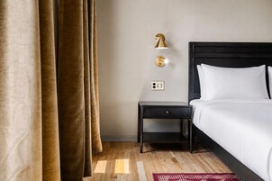 A hotel room with a bed, a nightstand, a wall-mounted lamp, and a power outlet.