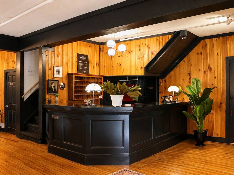 Un espace d’accueil avec un décor intérieur en bois, un comptoir d’accueil, un escalier et une plante en pot.