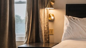 A hotel room with a bed, a nightstand, a lamp, and a window with curtains. - Hotel St. Moritz (Lake Placid)