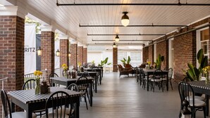 A covered outdoor dining area with brick walls, wooden flooring, and tables with chairs. - Hotel St. Moritz (Lake Placid)