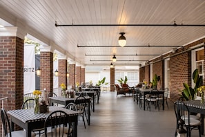 A covered outdoor dining area with brick walls, wooden flooring, and tables with chairs. - Hotel St. Moritz (Lake Placid)