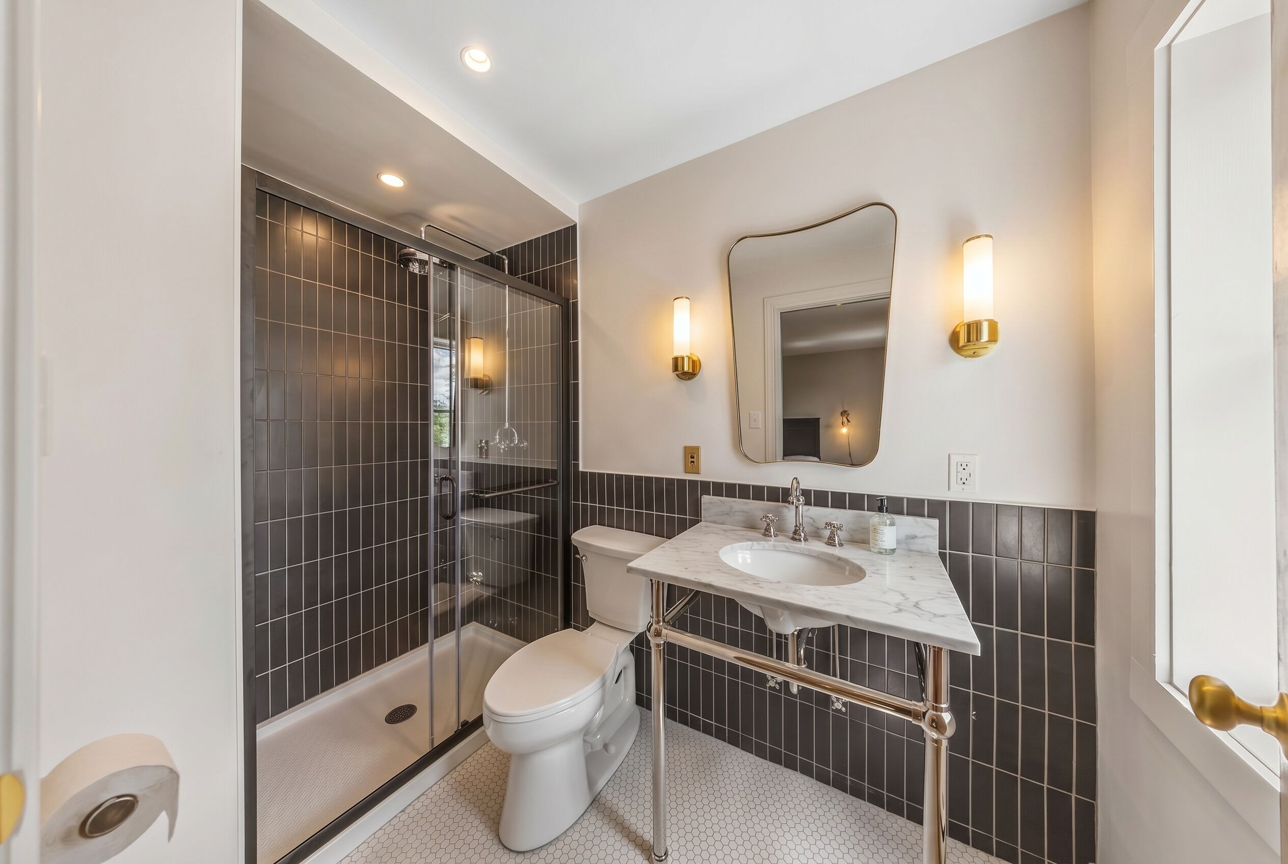A modern bathroom with a glass shower enclosure, a white toilet, a marble sink, and a mirror with wall sconces.
