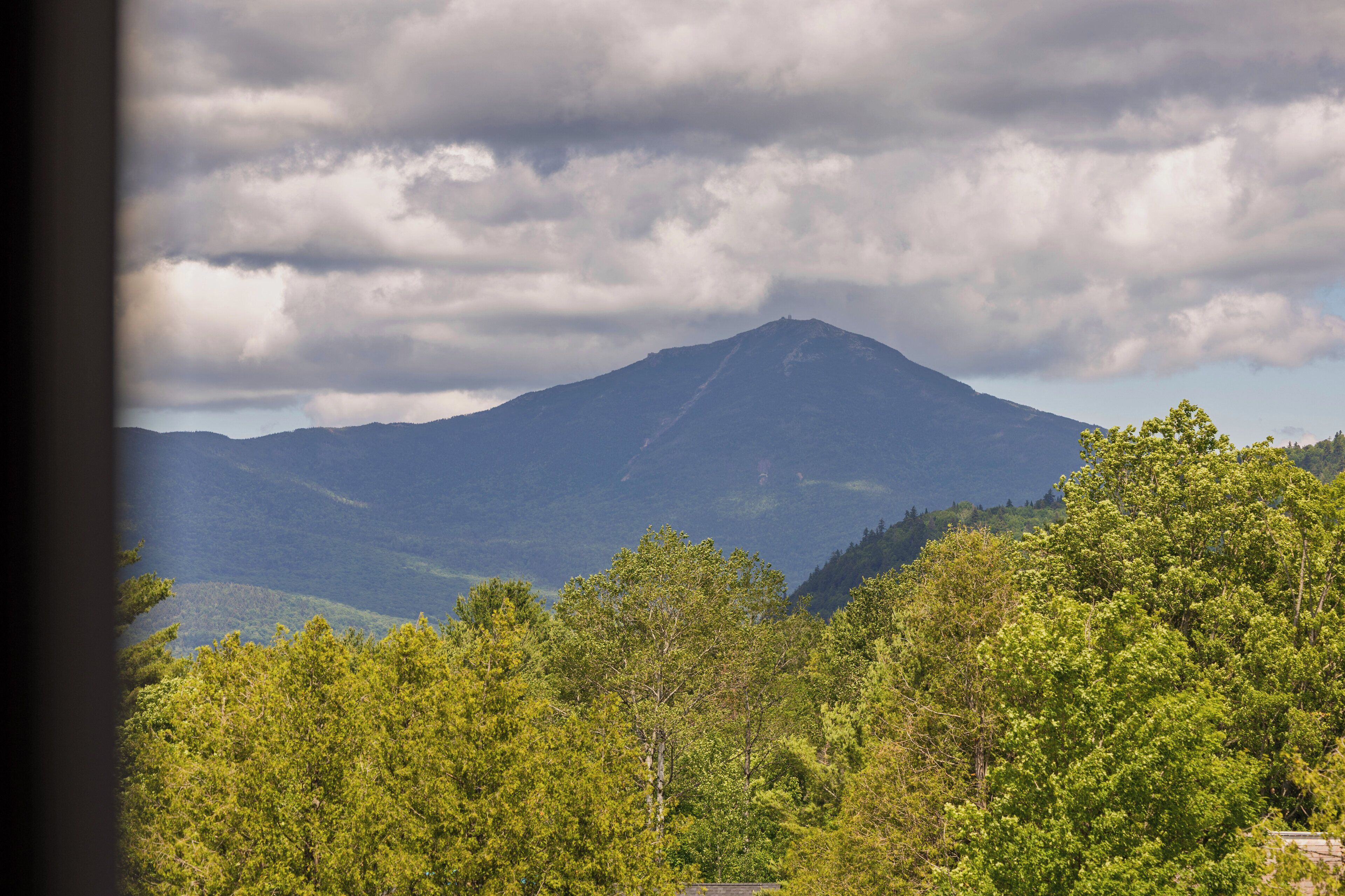 A mountain with a forested foreground and a cloudy sky.