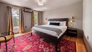 Une chambre à coucher moderne avec un grand lit, une chaise, une table de chevet et une fenêtre avec des rideaux.