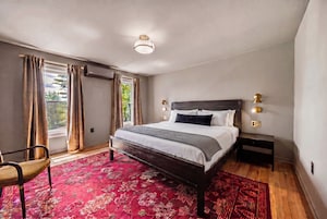 A modern bedroom with a large bed, a chair, a nightstand, and a window with curtains.