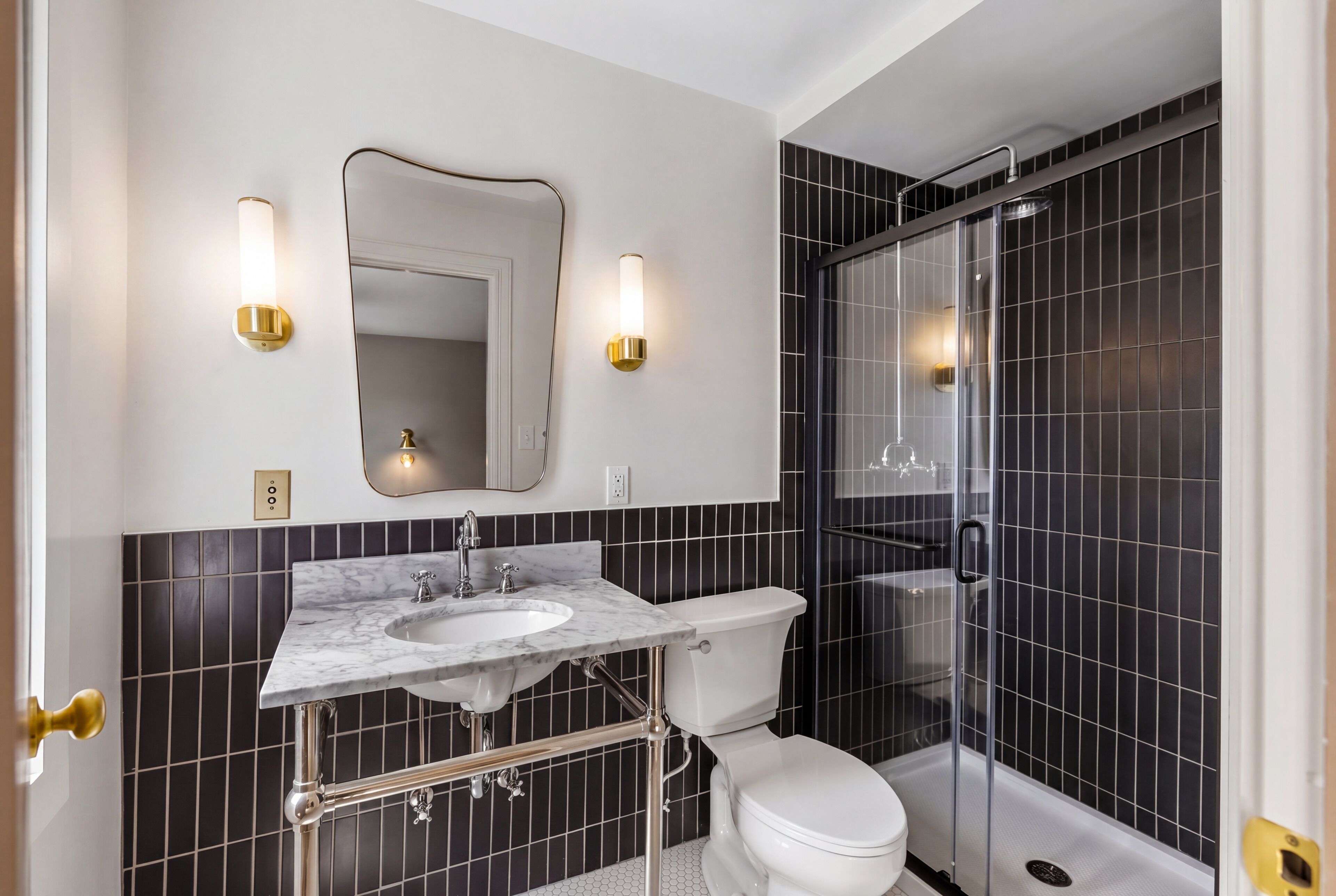 Een badkamer met een marmeren wastafel, toilet, douche met glazen wanden en zwart betegelde muren.