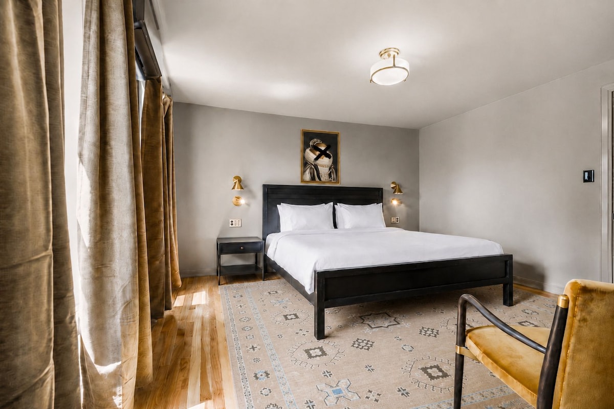A bedroom with a bed, nightstands, a chair, and a patterned rug.