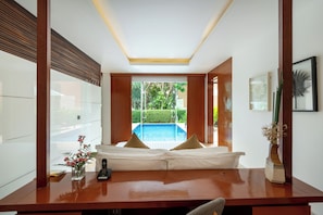 A modern hotel room with a wooden desk, a remote control, and a view of an outdoor swimming pool.