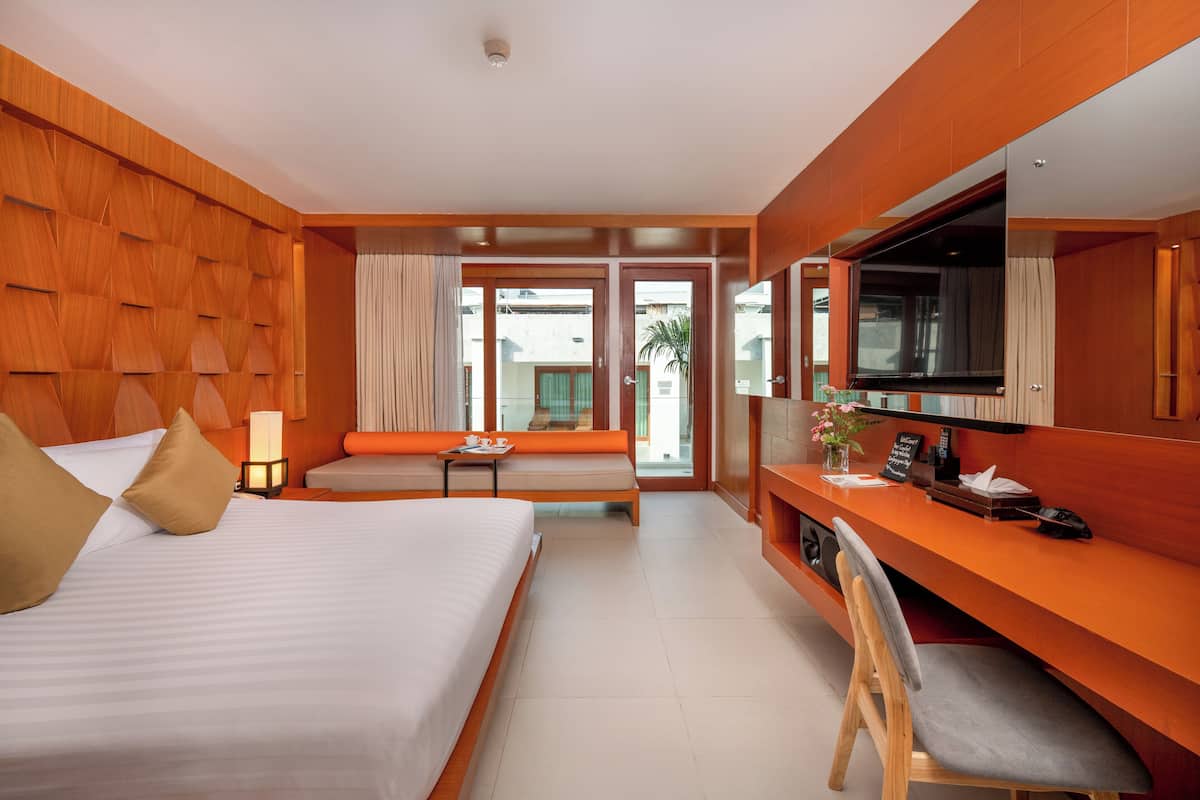 A hotel room with a large bed, a desk with a chair, a television, and a seating area with a view to the outside.