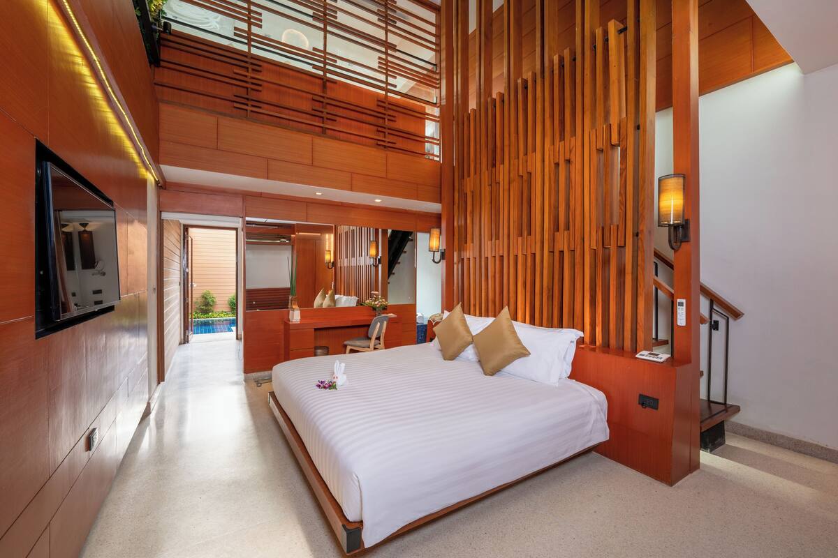 A modern hotel room with a large bed, wooden paneling, a desk, and a television.