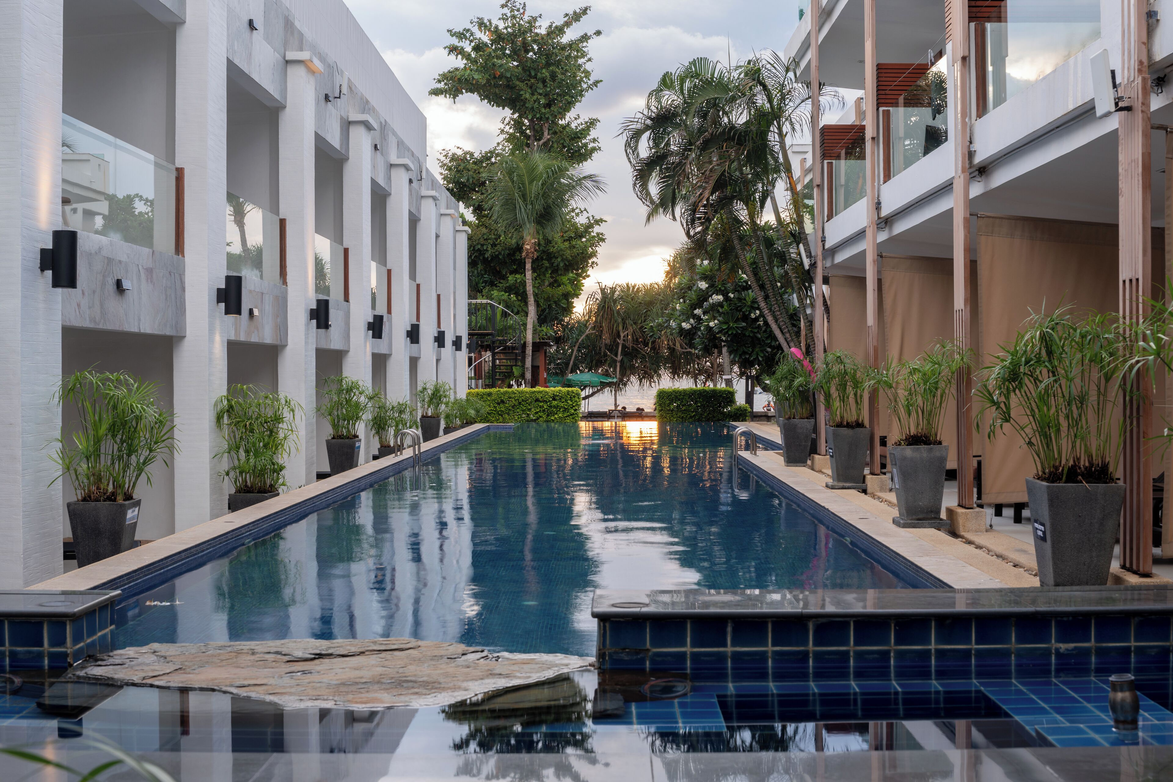 A swimming pool with a tiled edge, surrounded by potted plants and modern buildings with balconies.