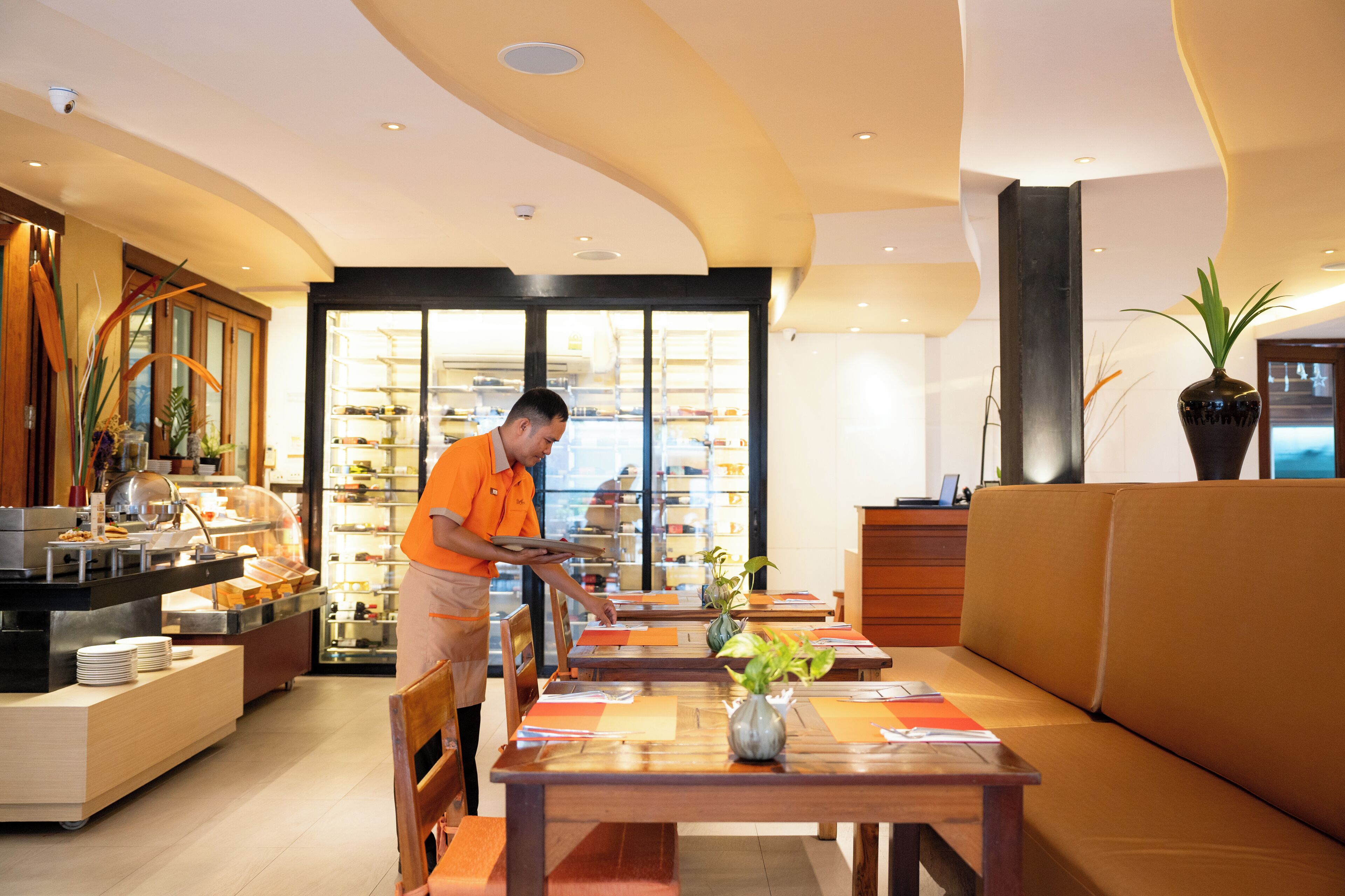 Un moderno vestíbulo de hotel con zona de buffet, mesas de madera y un área de estar.