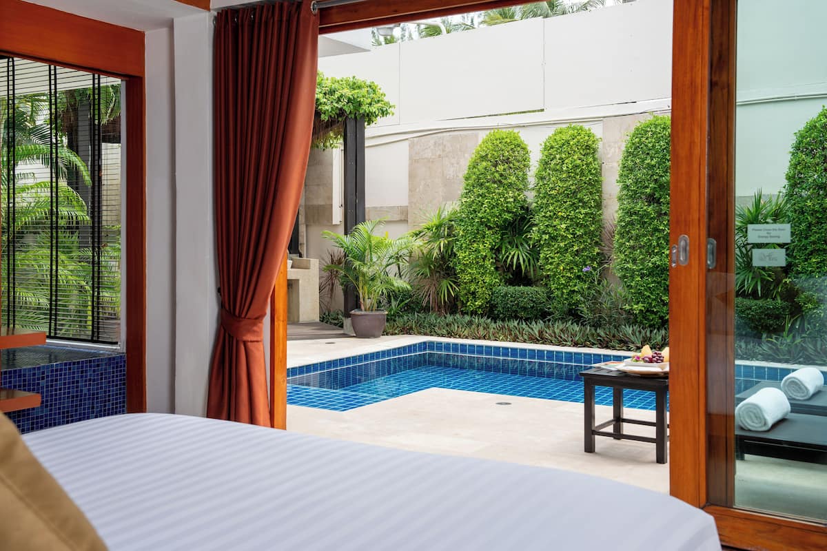Quarto com vista para uma piscina e vegetação.