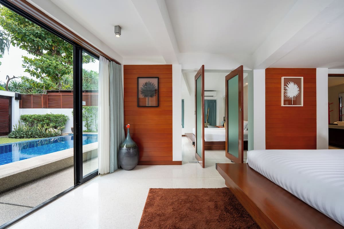 Quarto de hotel moderno com uma cama grande, vista para uma piscina e uma parede de destaque em madeira.