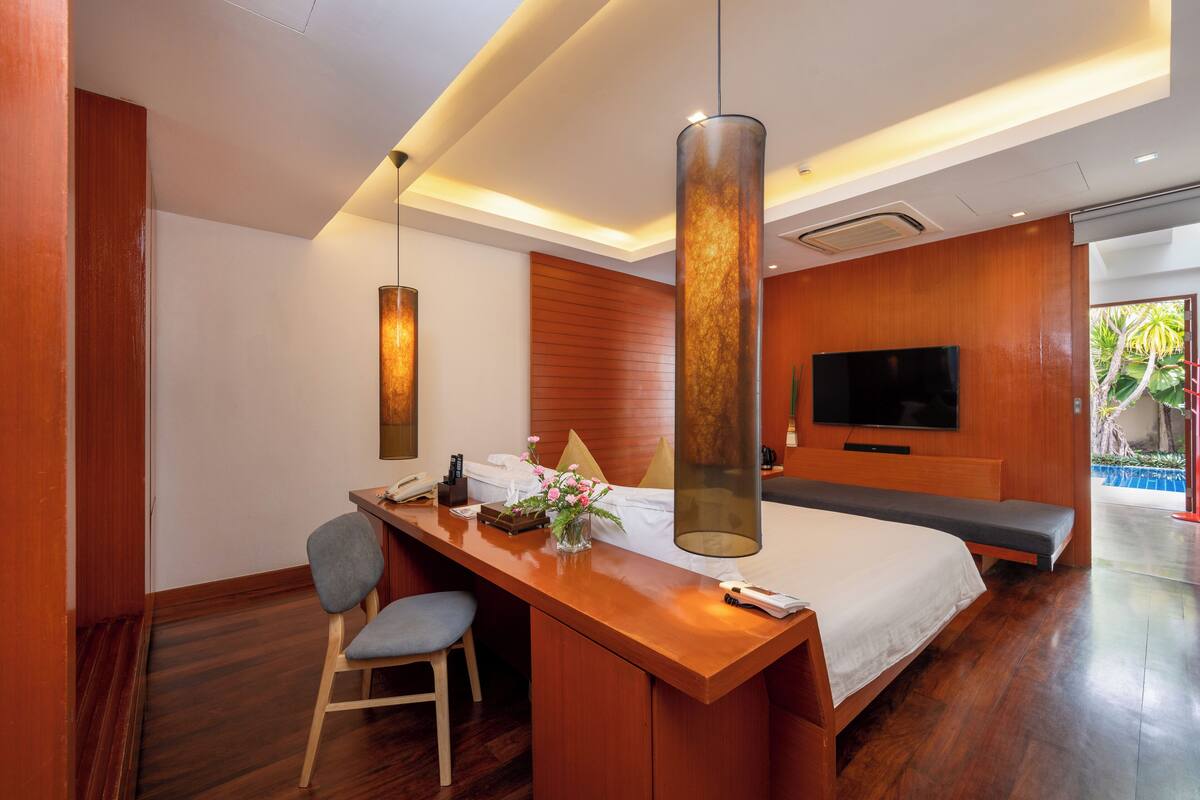 Quarto de hotel com escrivaninha de madeira, uma poltrona confortável, uma cama grande, televisão e vista para o exterior.